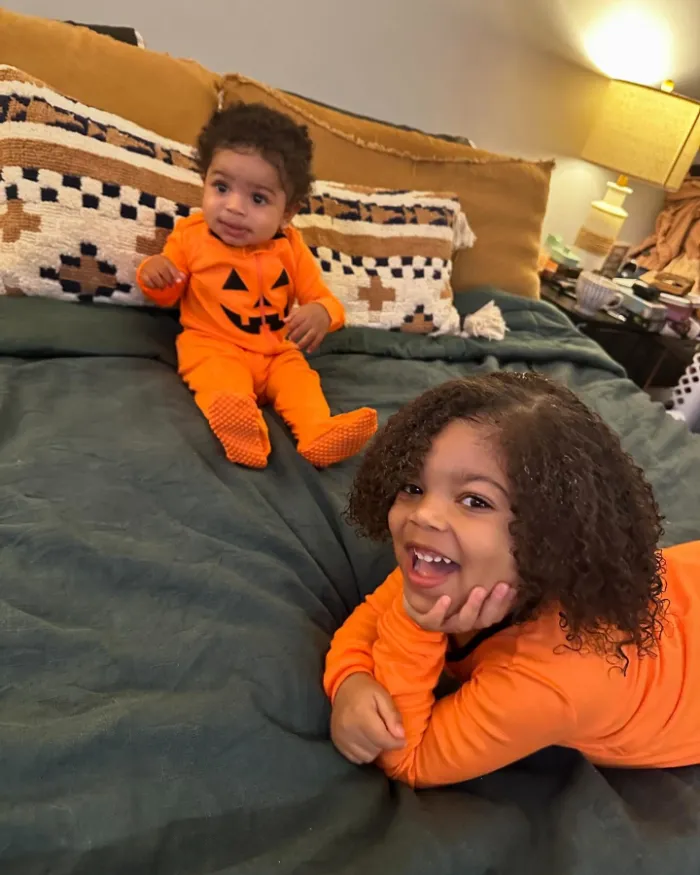 Siblings in matching pumpkin pajamas on a cozy bed.